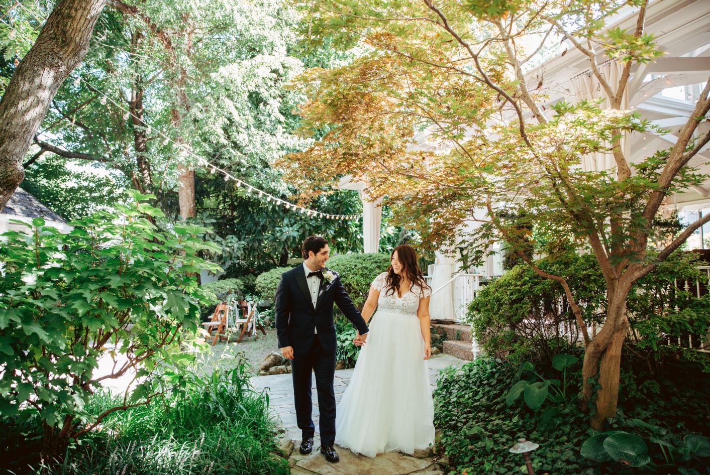 Bride and groom walking hand in hand through enchanted garden at their earthy summer garden wedding in September