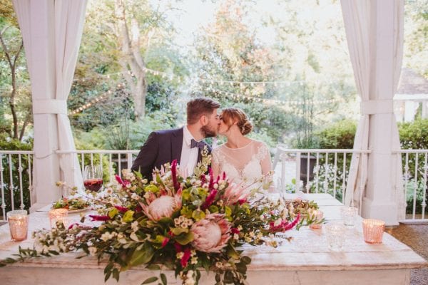 bride and groom kissing in a garden at sweetheart table